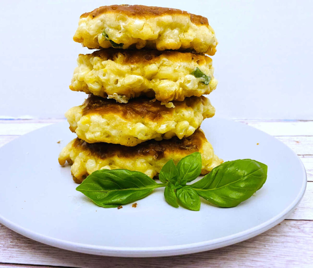 a tall pile of corn fritters sits on a white plate with a basil garnih. 