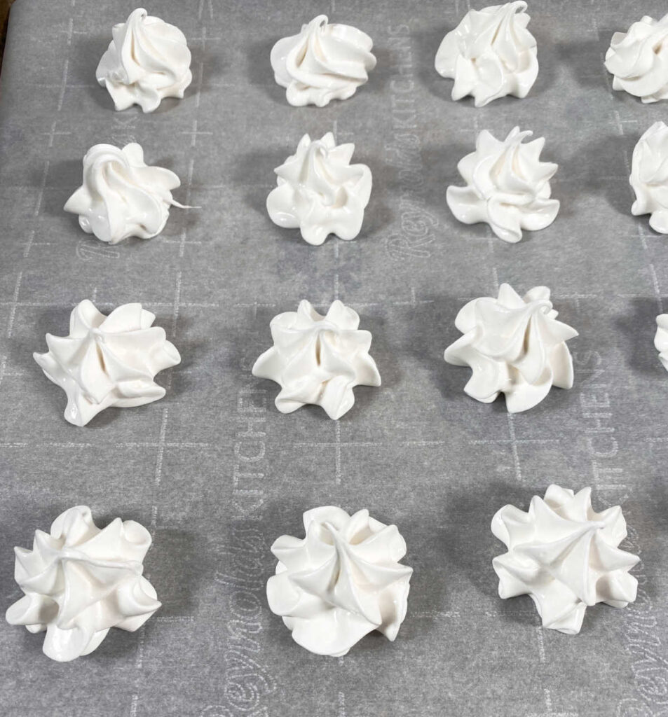 piped meringue cookies sit on parchment paper.