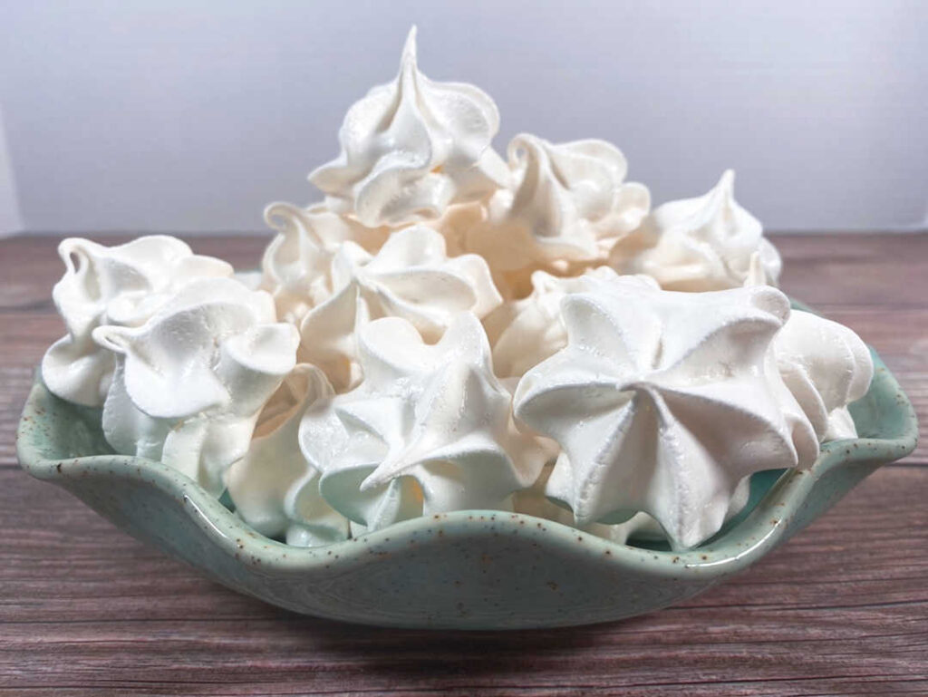 light green bowl of meringue cookies sits on a wooden background