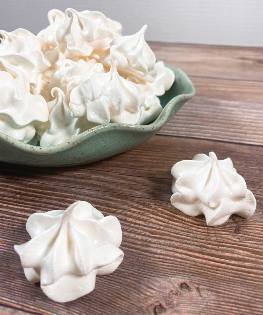 green bowl full of egg white cookies sits on a wooden background 