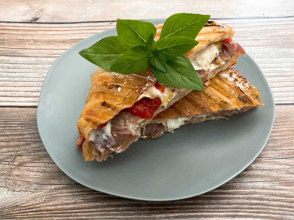 overhead image of the panini sliced in half and topped with a sprig of fresh basil 