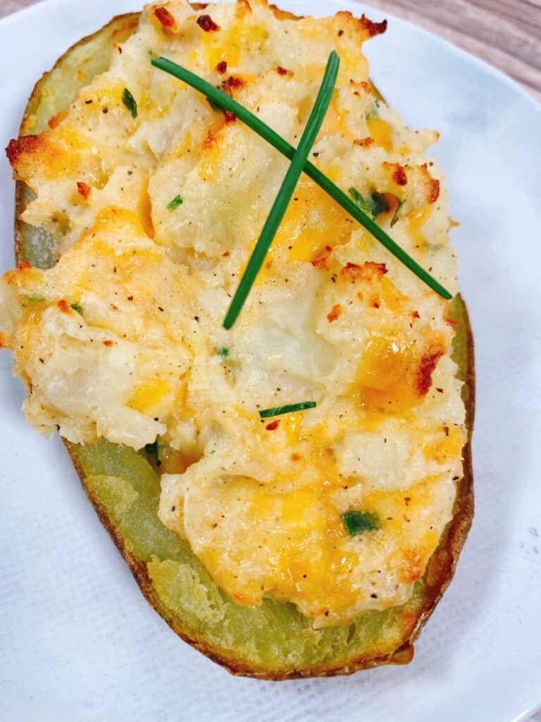 Close up image of a twice baked potato, showing the filling and the chive garnish.