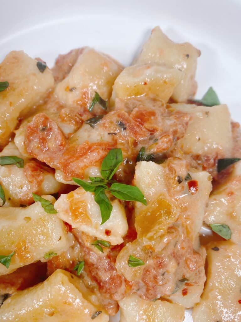 close up image of the recipe, showing the golden brown gnocchi after being pan fried, the creamy sauce on top and the fresh basil garnish.