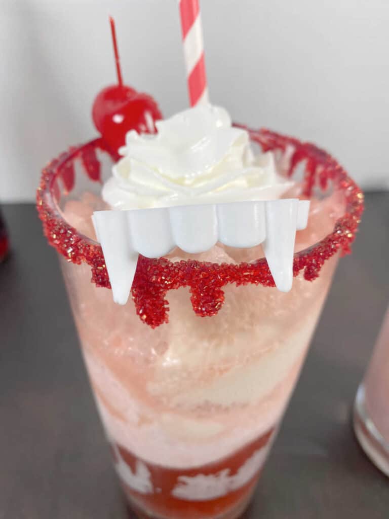 close up of float, with the blood rimmed glass and fake vampire teeth hanging over the edge of the glass. 