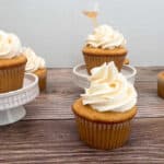 cupcakes sit on a wooden background and on white cupcake stands.