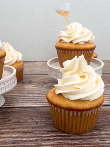 cupcakes sit on a wooden background and on white cupcake stands.