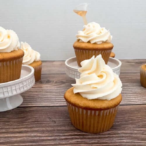 cupcakes sit on a wooden background and on white cupcake stands.