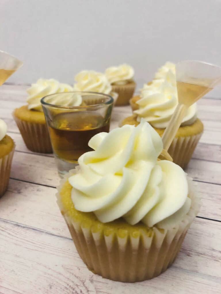 close up image of a cupcake, with a Shot Top filled with bourbon, in the frosting. Other cupcakes sit behind it. 