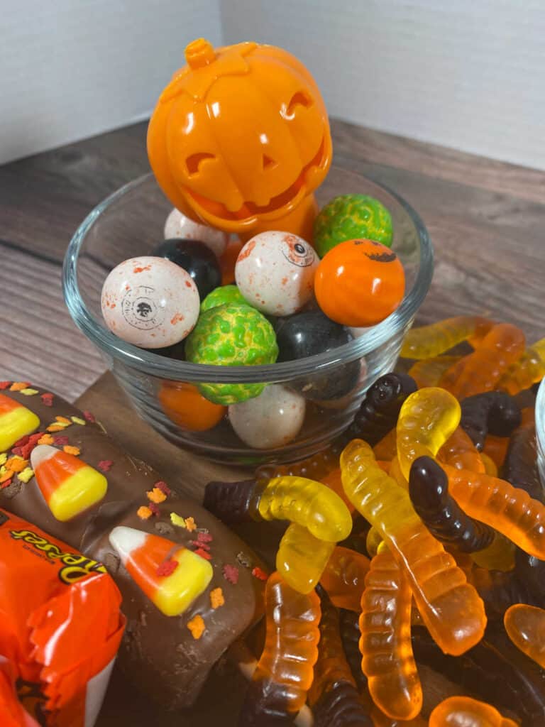 close up image of the halloween colored gumballs and gummy worms on the board. 