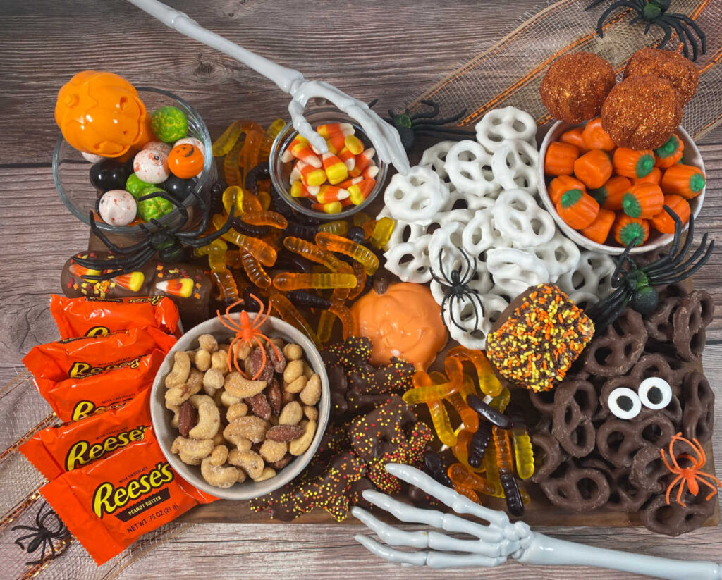 overhead image of the board decorated with halloween treats. Around the board is decorated with fake spiders and skeleton hands.