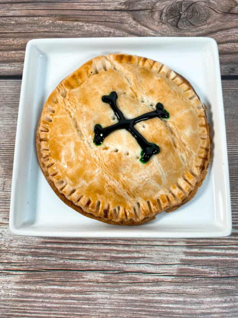 hand pie decorated with a cross bones sits on a square white plate on a wooden background 