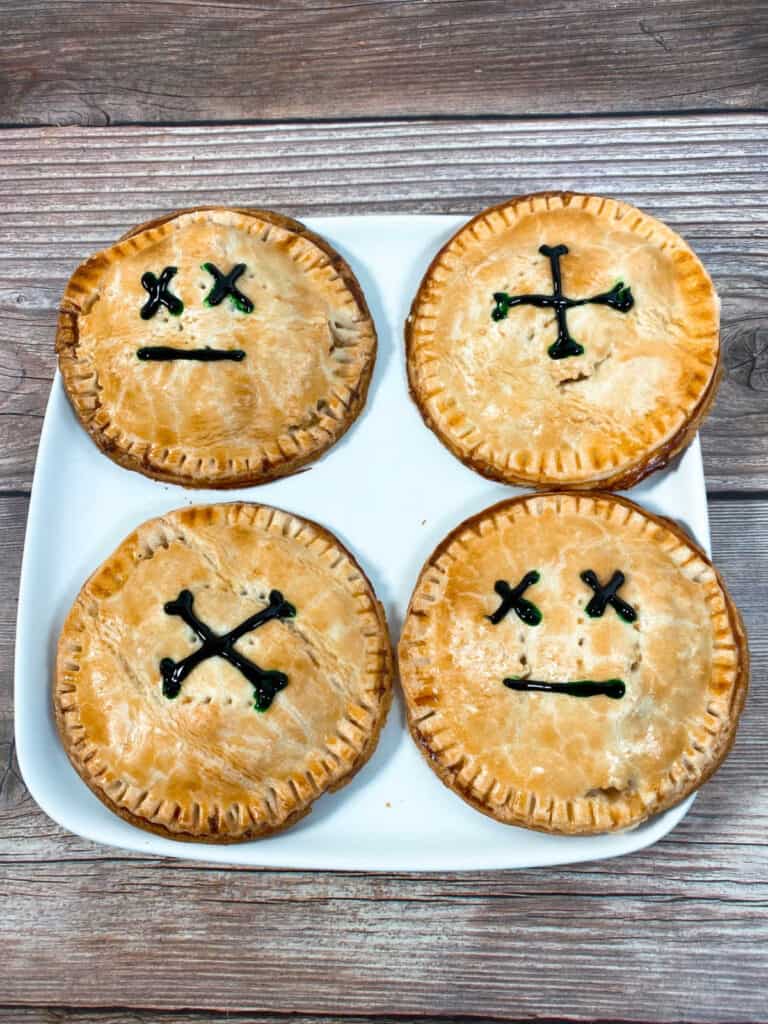 hand pies decorated to indicate they're poisonous sit on a square white plate on wooden background. 