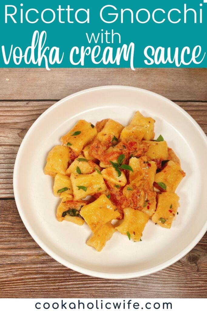 Image for Pinterest with text overlay at top. Bowl of gnocchi tossed in the vodka cream sauce is garnished with fresh basil and sitting on a wooden background.