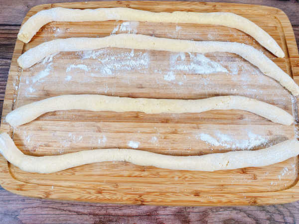 Process Shot - 4 ropes of the gnocchi dough sit on a wooden cutting board. 