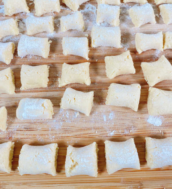 Process shot - close up image of the gnocchi cut into pieces, sitting on a wooden cutting board. 