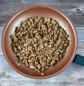 process shot - a skillet of seasoned ground turkey, garlic and onions sits on a wooden background. 