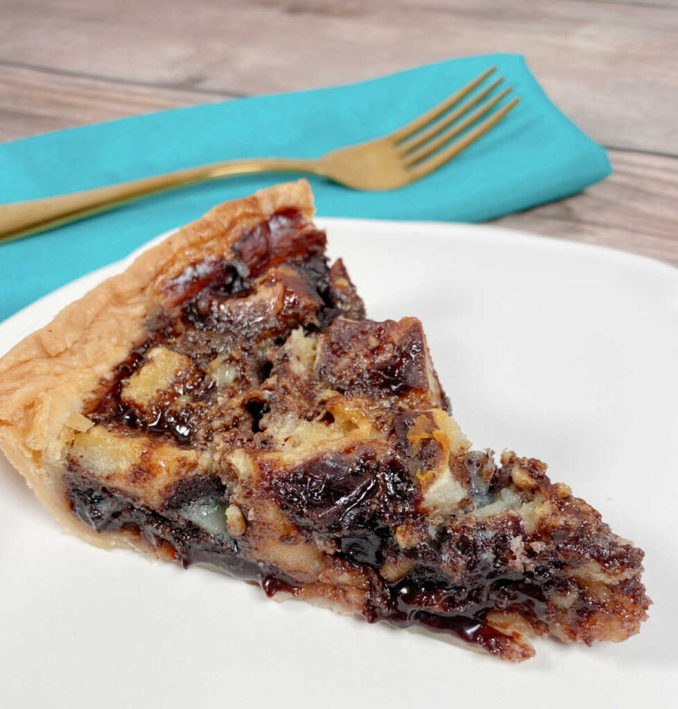 Slice of pie, showing off the melted chocolate center sits on a white plate with a gold fork in the background. 