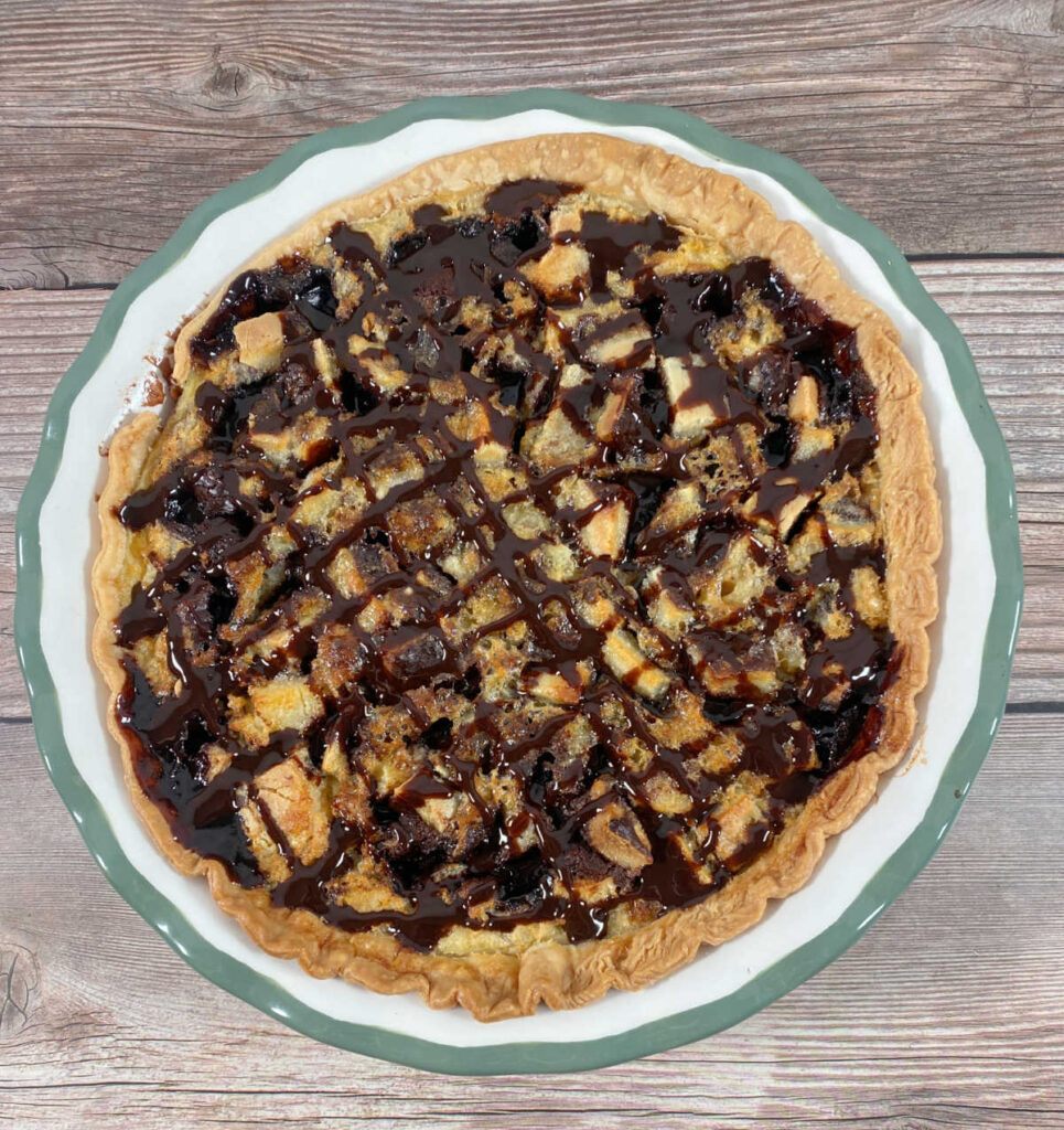 overhead image of whole pie, drizzled with chocolate syrup, sits on a wooden background. 