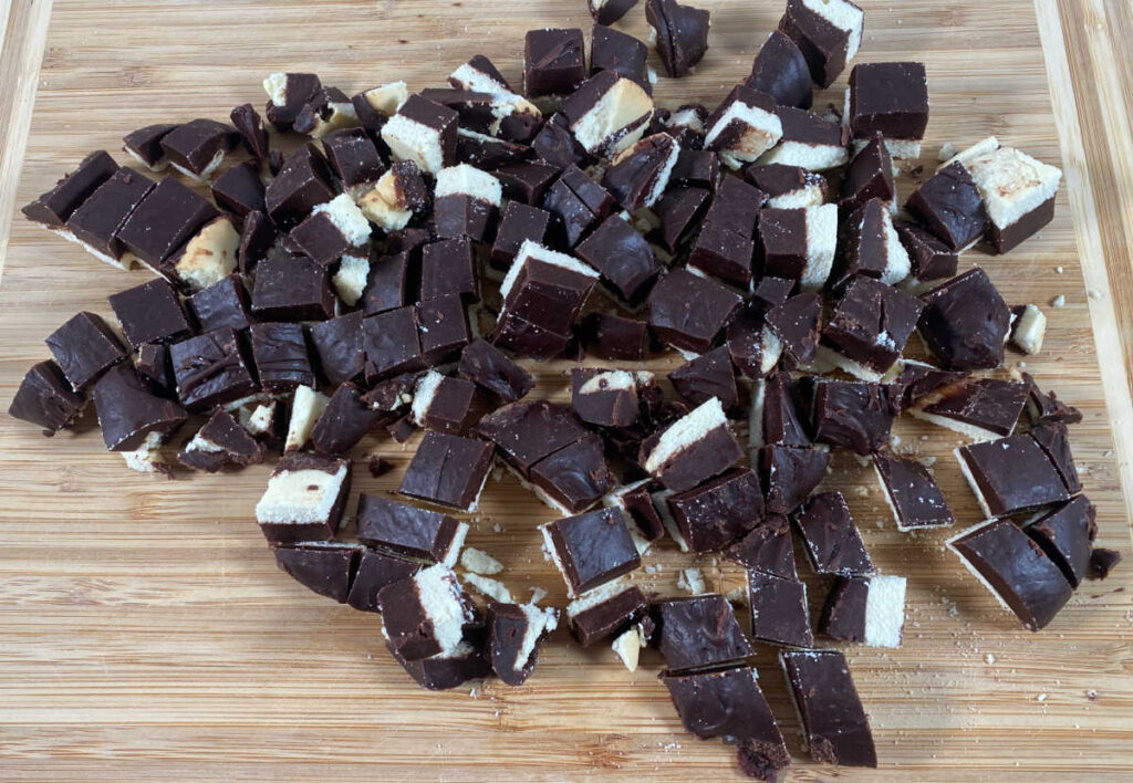 Process shot - Berger cookies are chopped up on a wooden cutting board. 