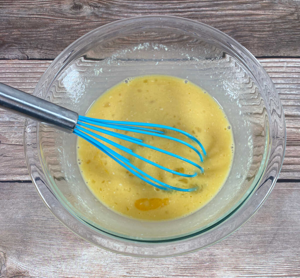 Process shot - remaining ingredients are whisked together in a glass bowl. A blue silicone whisk is still in the bowl. 