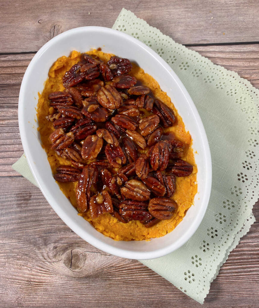 topped sweet potatoes sit in a white, oval dish on a wooden bacground. 