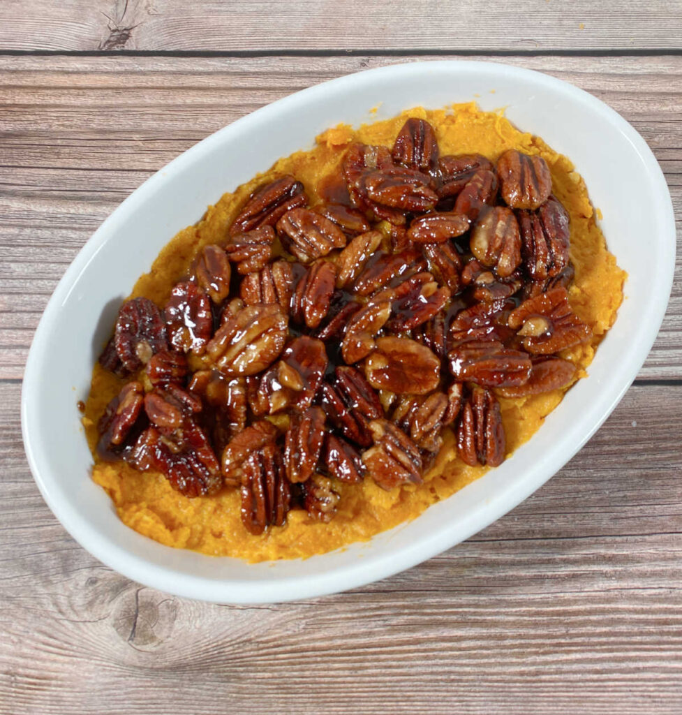 process shot - mashed sweet potatoes transferred to a white dish, topped with the coated pecans. 