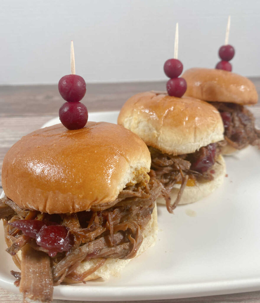 three sliders, garnished with cranberry toppers, sit in a diagonal row on a white plate.