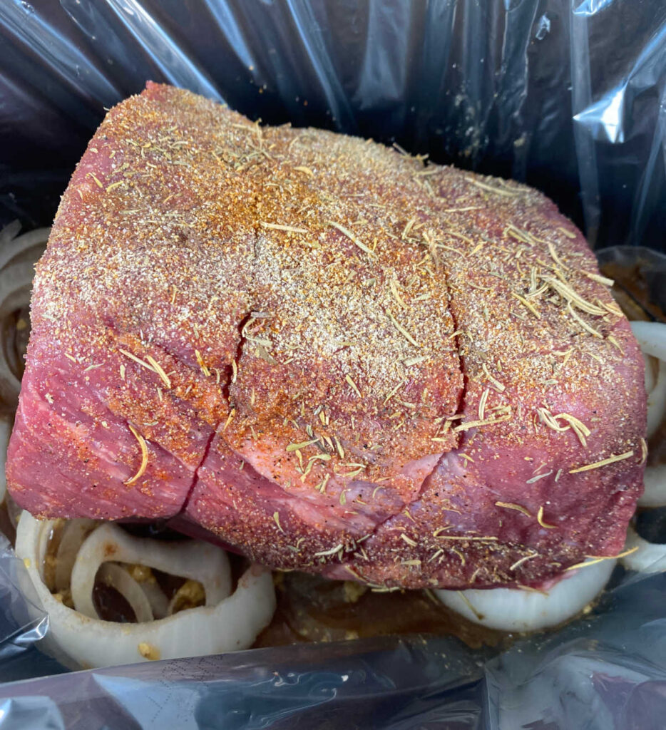 process shot - beef roast, seasoned with spices sits on top of the onions in the slow cooker. 