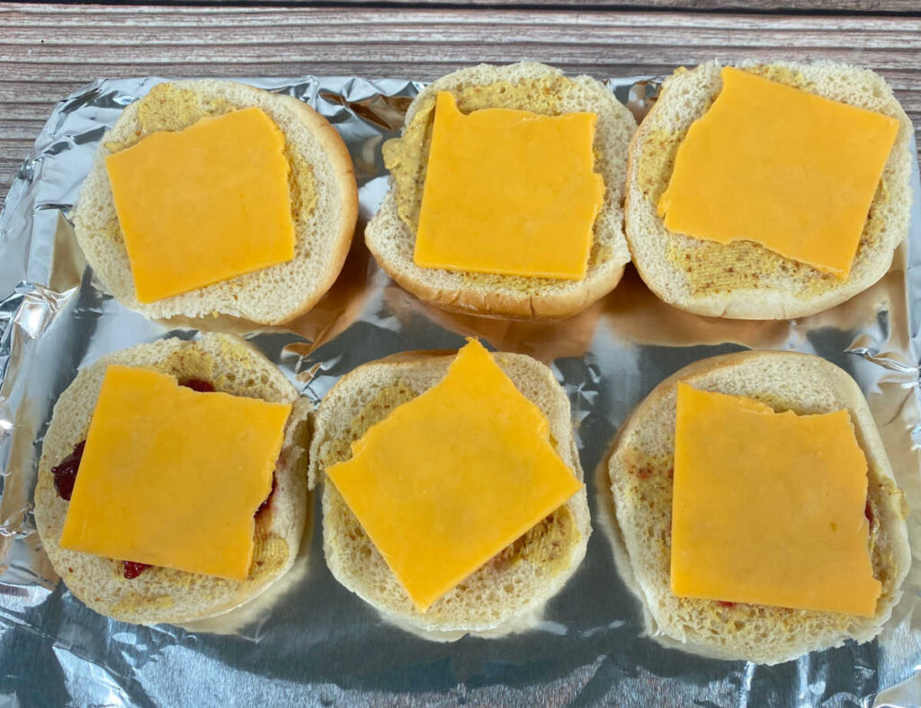 process shot - slider buns are spread with mustard, topped with cheese and ready to be toasted. 