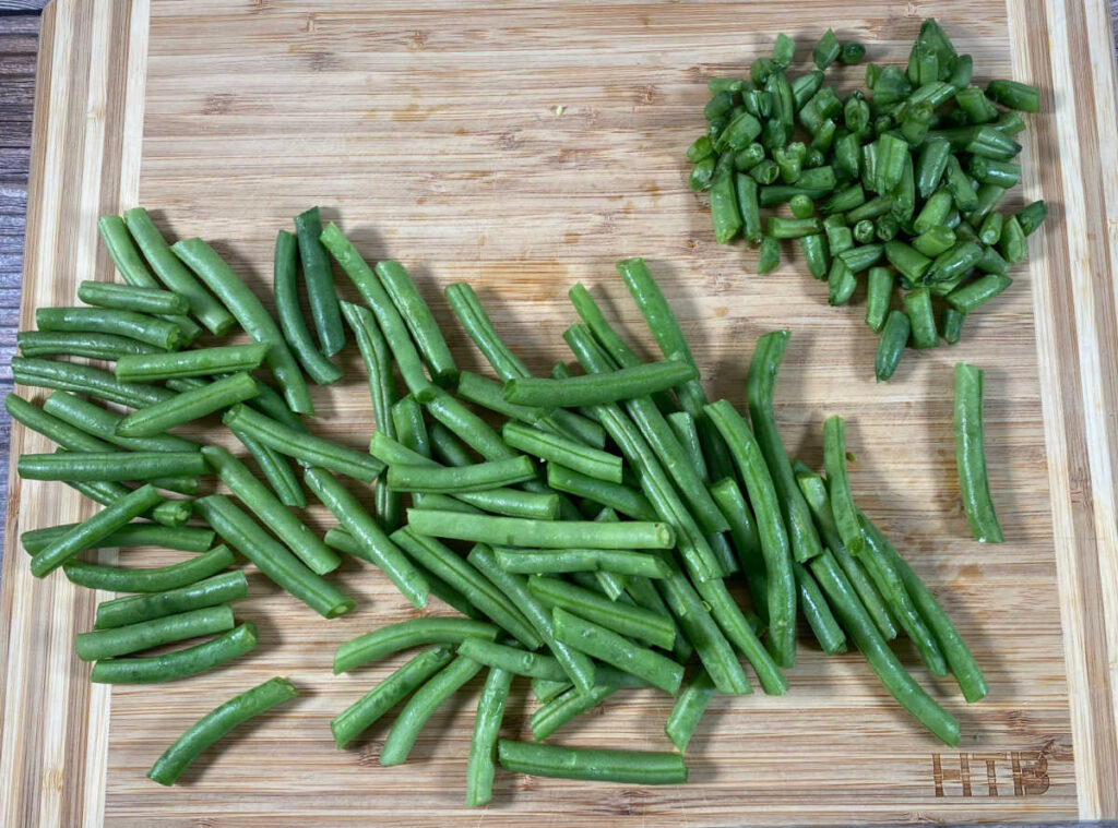 process shot - trimmed green beans sit on a wooden cutting board. 