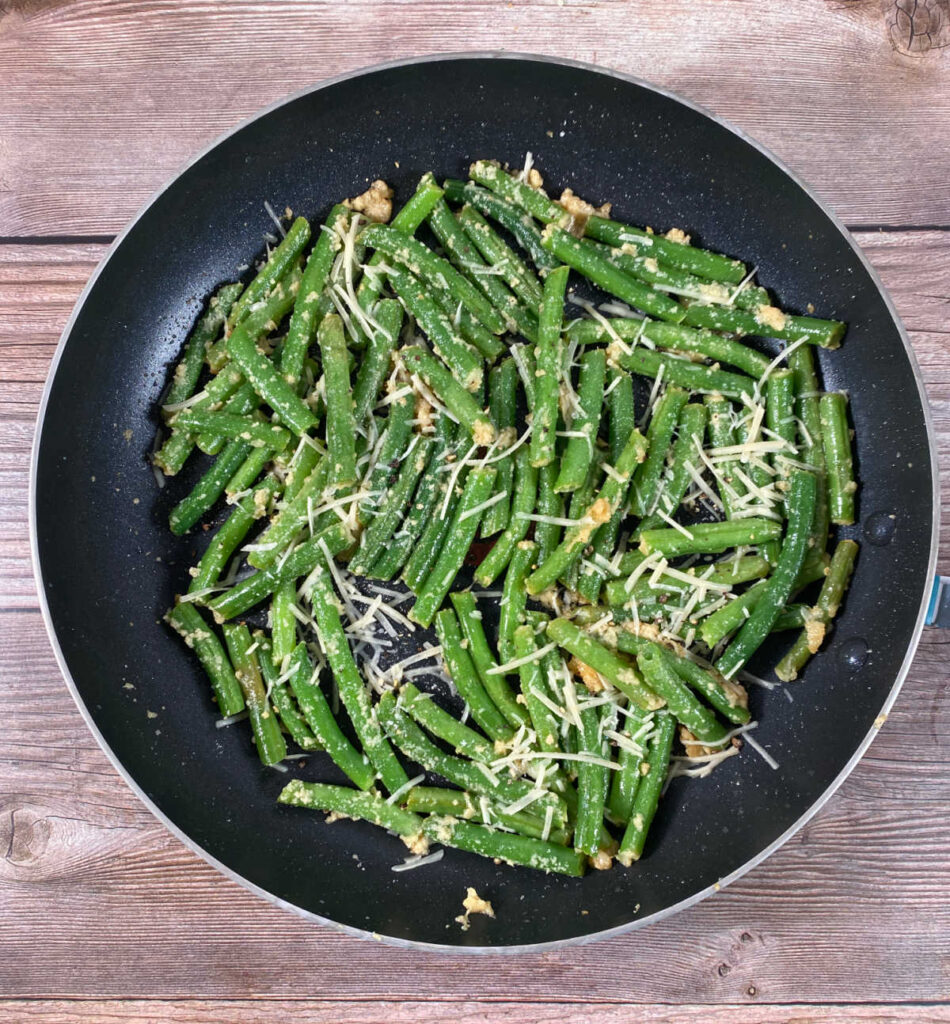 green beans, topped with parmesan cheese, sit in a black skillet. 