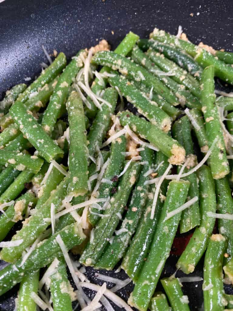 final process shot - green beans and garlic in a skillet topped with parmesan cheese 