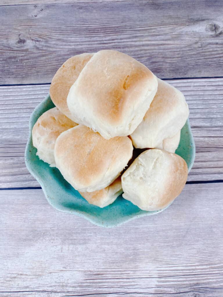 a pile of rolls sit in a round turquoise dish on a wooden background. 