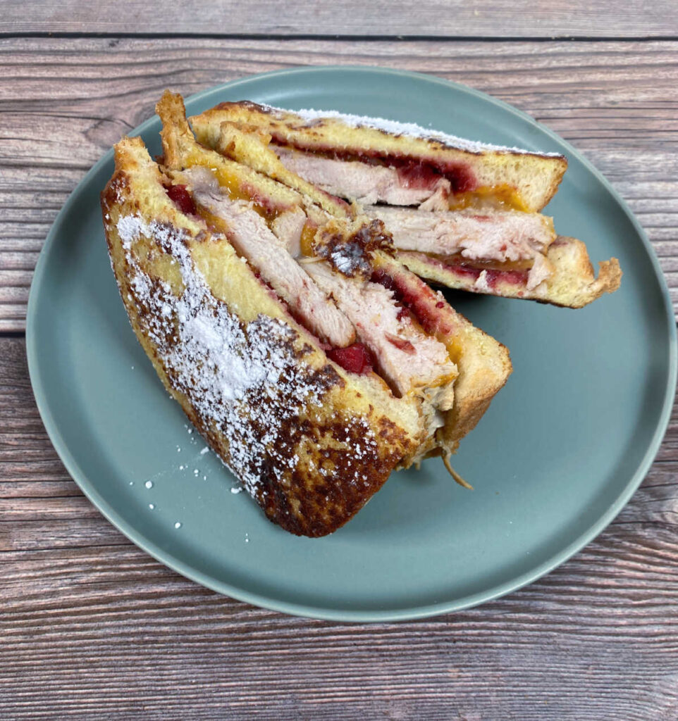 Crispy sandwich, showing off the powdered sugar topping, is sliced in half and standing upright to reveal ingredients inside.