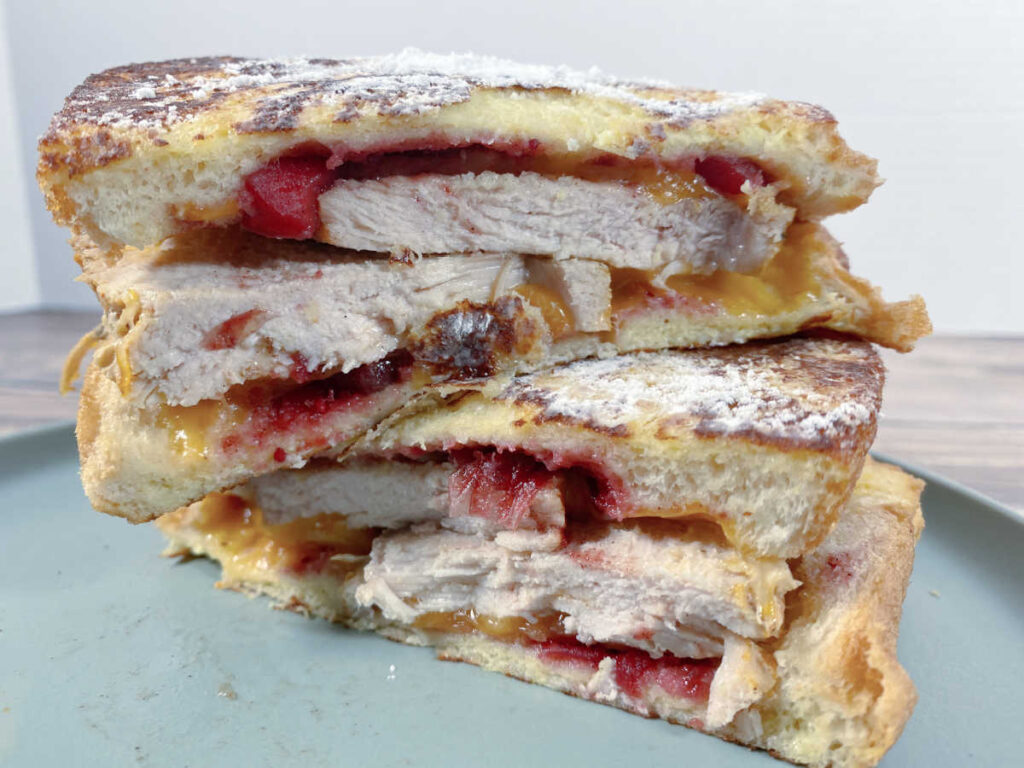 Halved sandwich, stacked on top of each other shows ingredients inside and the crispy, powdered sugar covered top. 