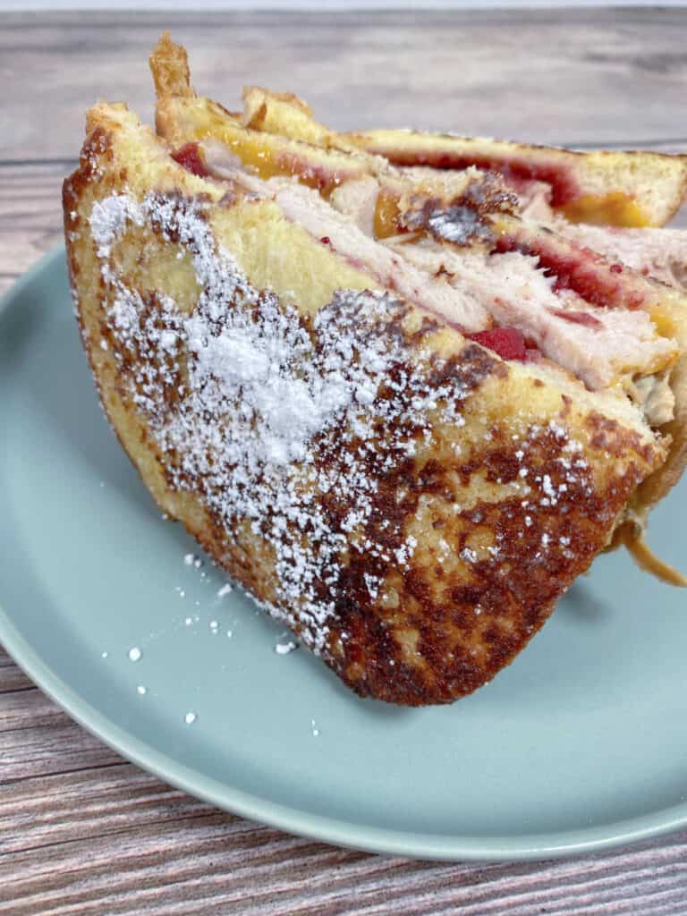 Halved sandwich, dusted with powdered sugar, is standing upright to show turkey, cheese and cranberry sauce inside.