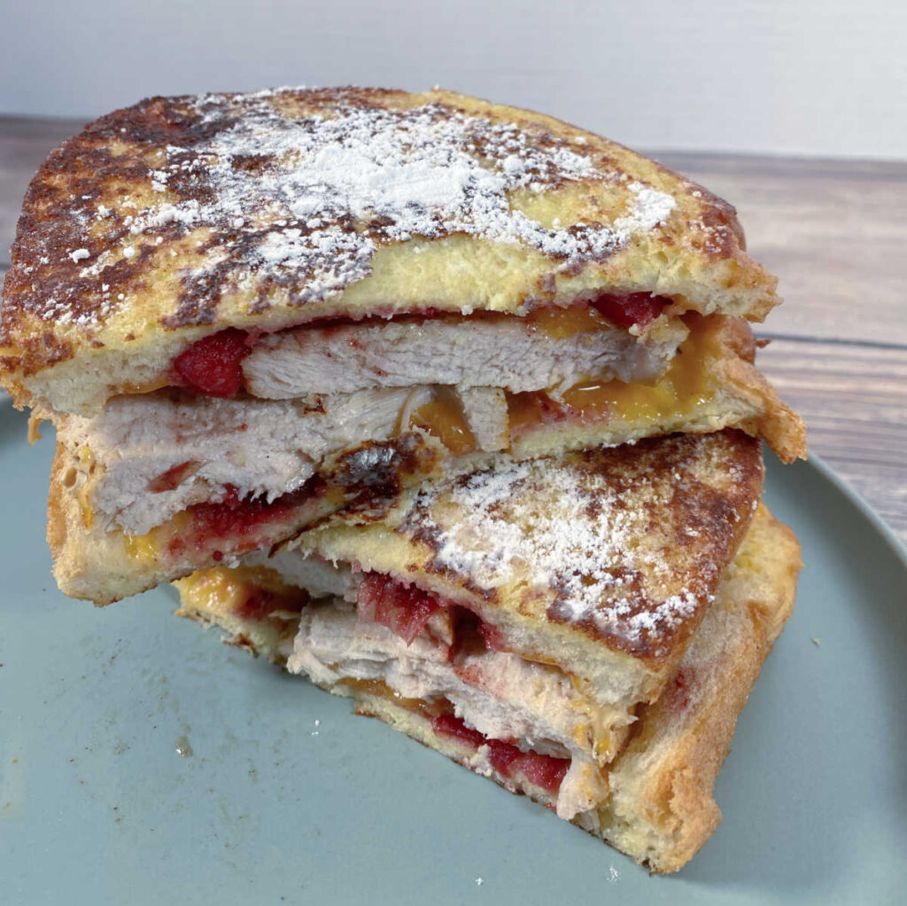 Cooked sandwich, sliced in half and stacked on top of each other to show the ingredients inside. 