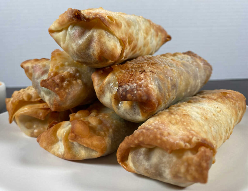 Process shot - pyramid of air fried egg rolls sits on a white round plate. 