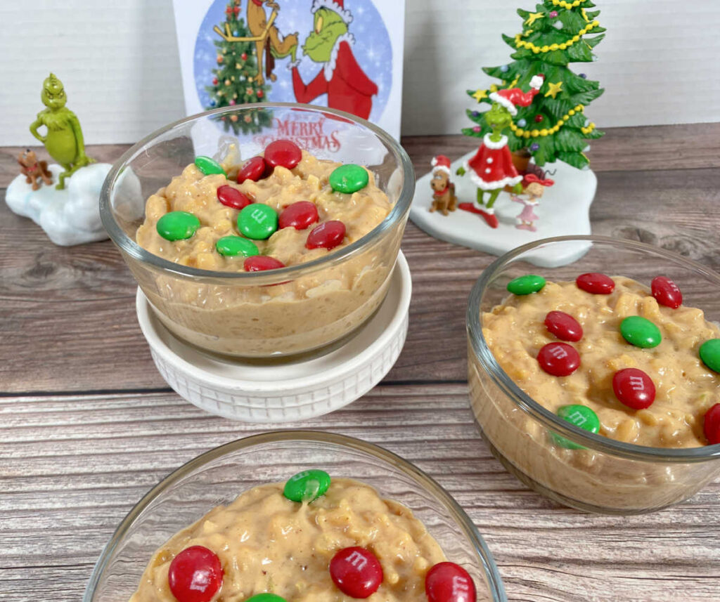 Bowls of pudding, placed at various heights, sit on a wooden background with Grinch decor. 