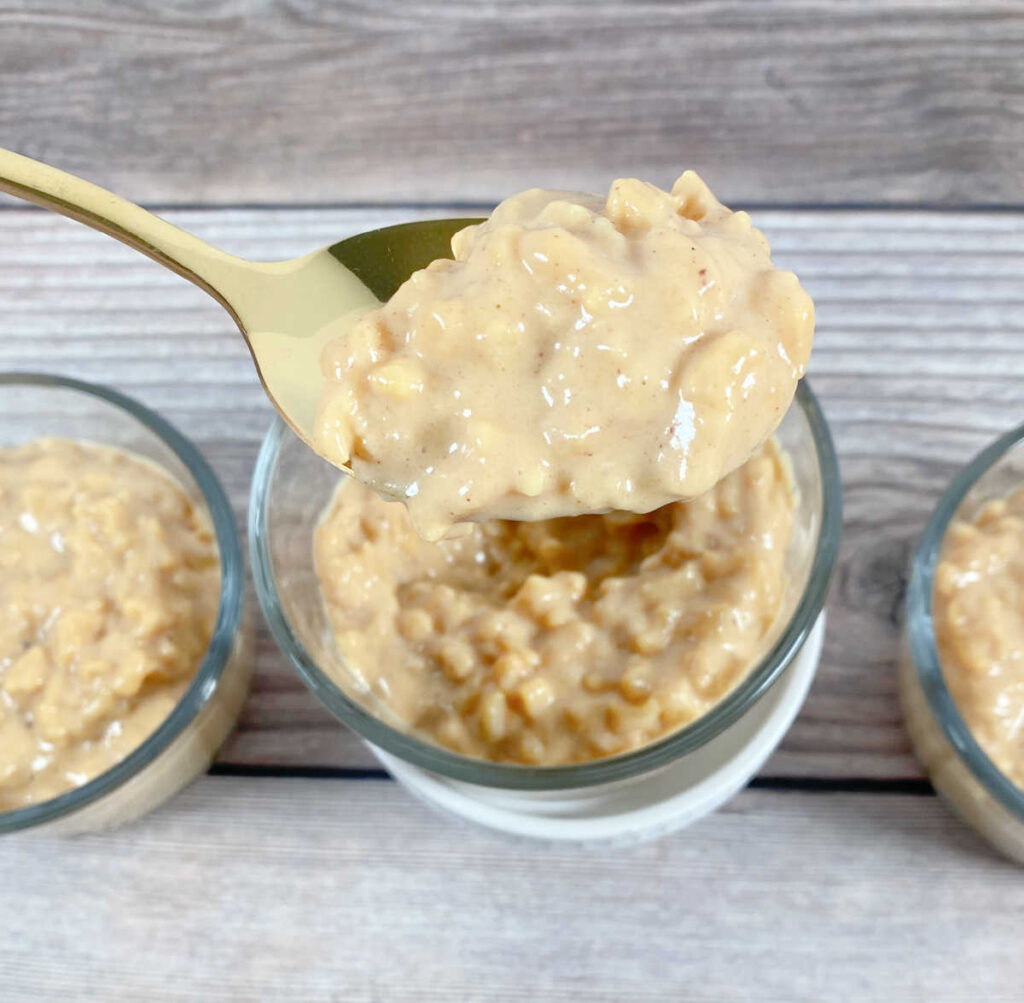 Process shot - ramekins are filled with pudding, a spoon lifts up the last of the rice pudding to add to the ramekin. 