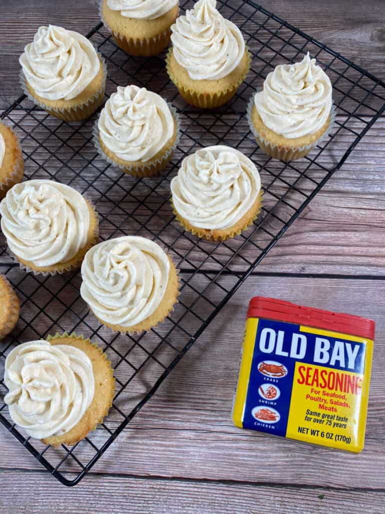 frosted cupcakes sit on a wire rack with a can of old bay seasoning next to them. 