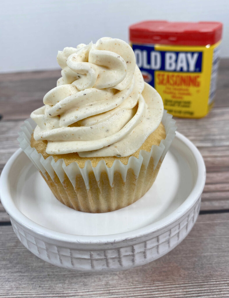 Close up image of cupcake sitting on a white cupcake stand with a can of old bay in the background. 