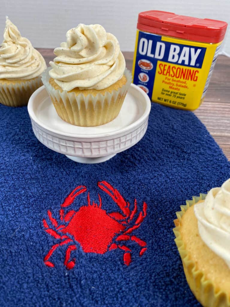 cupcakes sit on a blue kitchen towel with a crab design. Can of old bay seasoning sits in the background.