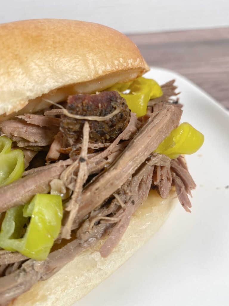 Close up image of sandwich on a white plate, showing the shredded beef and peppers. 