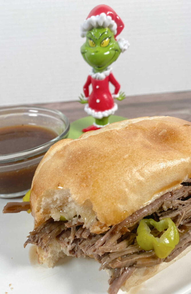 Close up of sandwich with a bite missing, bowl of gravy in the background a Grinch figurine. 