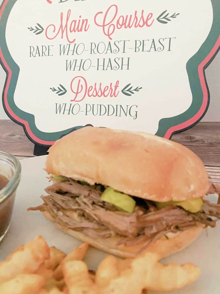 Close up image of sandwich and gravy on a plate. In the background sits a menu showing Roast Beast as part of the Who's Christmas Dinner menu. 