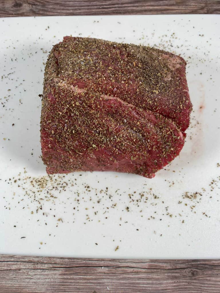 Process shot - beef roast sits on a cutting board covered in seasonings, waiting to be seared. 