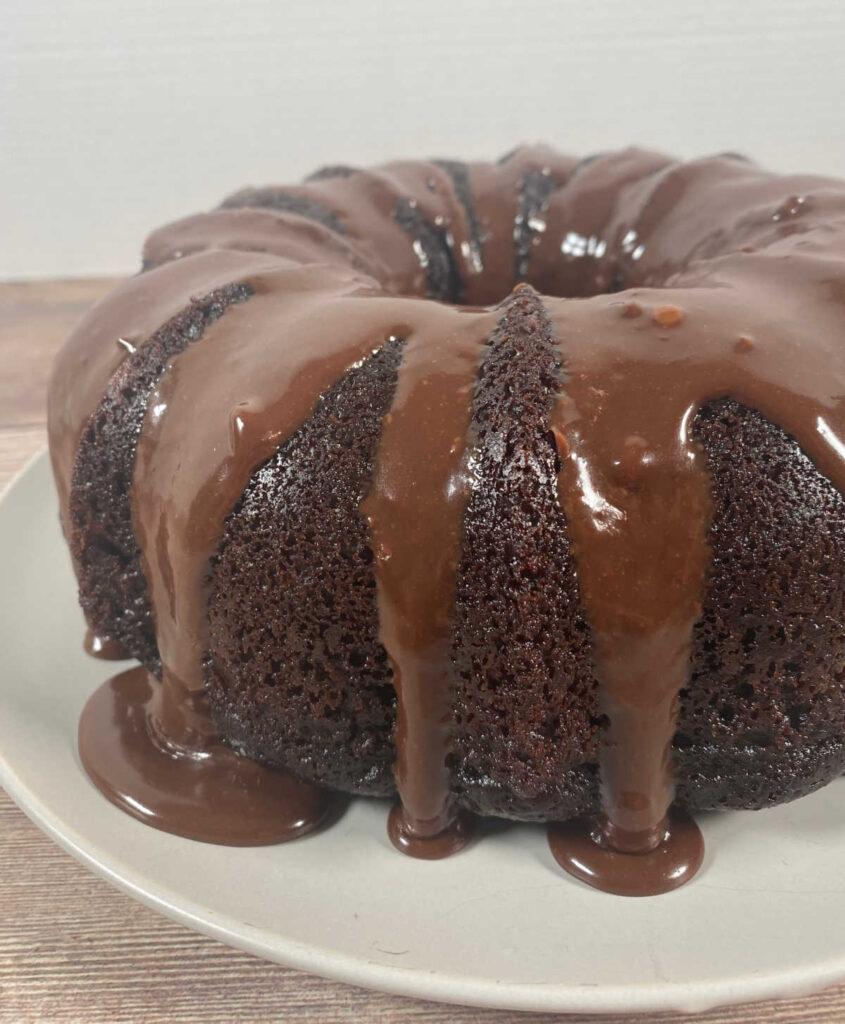 Bundt cake on a white plate with chocolate glaze dripping down the sides. 