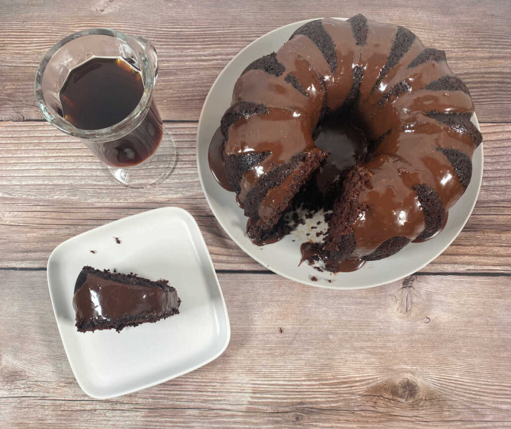 slice of cake, full cake and glass cup of coffee sit on a wooden background. 