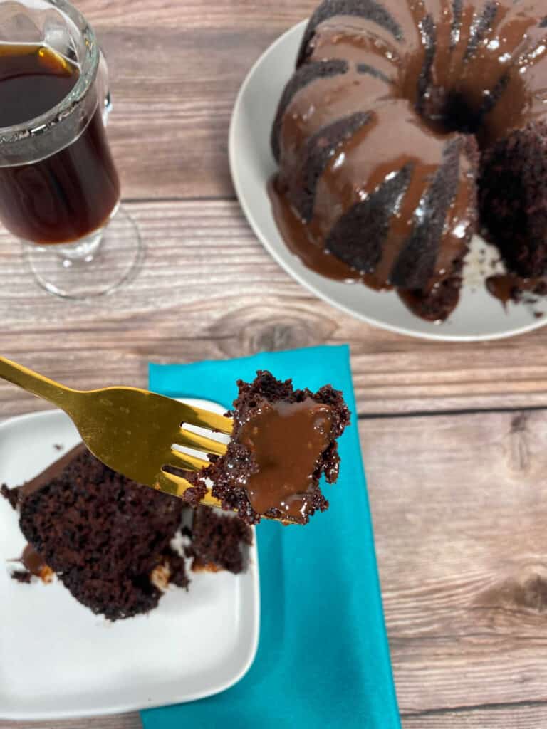 Piece of cake on a gold fork hovers above slice of cake and a glass of coffee. 